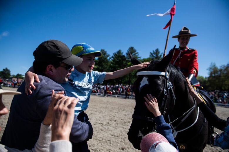 Children reach out to pat a horse while an RCMP officer smiles.