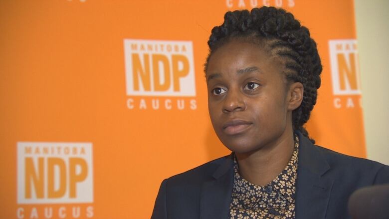 NDP MLA Uzoma Asagwara sits in front of a backdrop banner with the NDP logo on it.