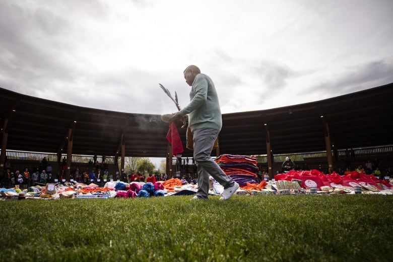 A man smudges donations laid in a grassy field inside an arbour on an overcast day.