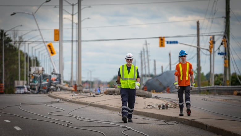 Men in reflective vests walk down a street with downed wires behind them