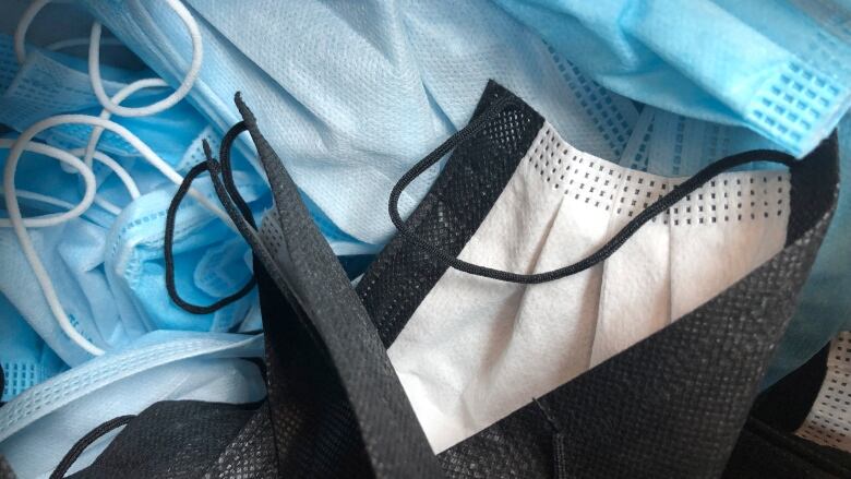 Blue and black surgical masks are shown in a messy pile on top of each other.