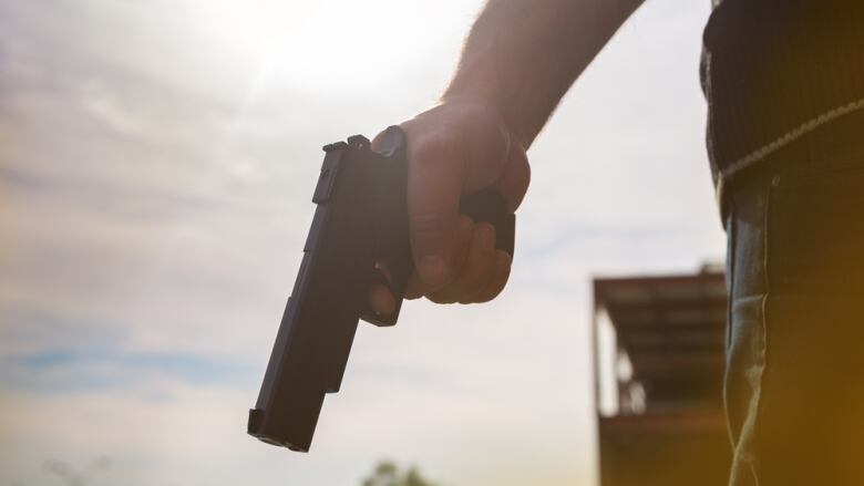 An arm holds a handgun on a sunny day.