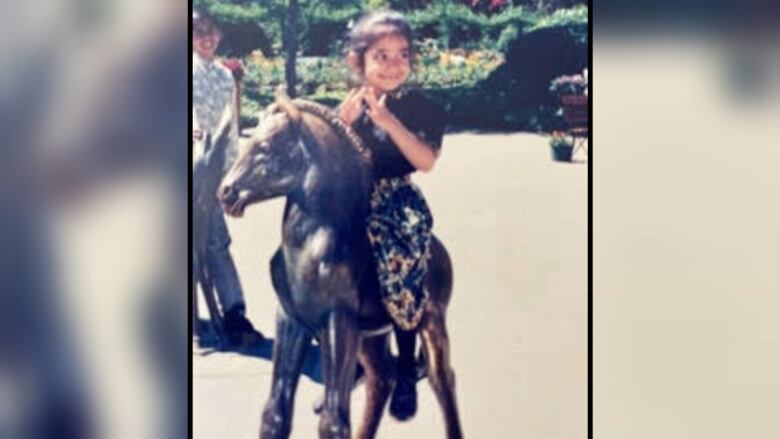 A smiling child sits on a horse statue. 