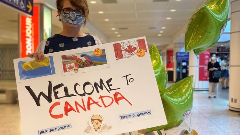 A woman holds a sign at a Montreal airport. The sign welcomes arrivals from Ukraine. 