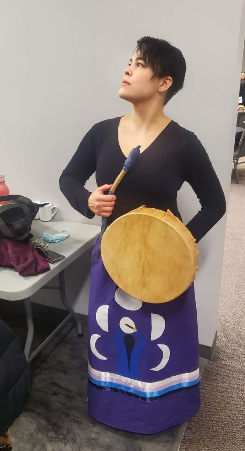 Julianna Maggrah in a ribbon skirt with a drum before a performance with the Spirit Strong Singers drum group.