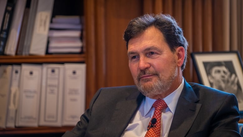 A bearded man in a suit sits in an office.