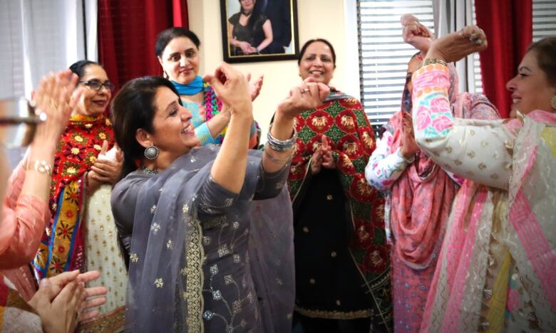 A group of Punjabi women are dancing with their hands raised in front of their faces. 