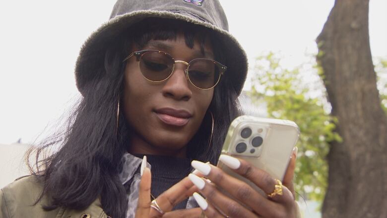 Kissy Duerre looks at her phone in a Saskatoon park. The Black, transgender woman, who is also a TikTok star, has faced racism and transphobia on dating apps.