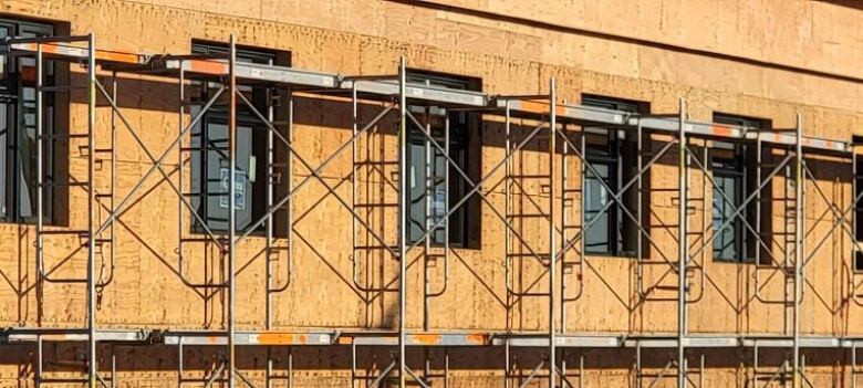 A close-up image shows windows behind metal scaffolding on a building clad in plywood. A photo taken from the website of the Ladysmith Resources Centre Association shows the 'Heart on the Hill' affordable housing development under construction.