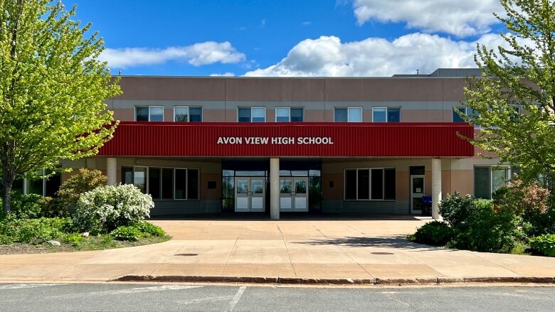 The outside of a school is seen, flanked by bushes and trees.