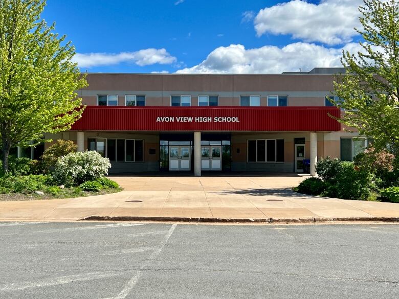 The outside of a school is seen, flanked by bushes and trees.