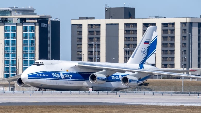 Massive Russian cargo jet sits parked on the tarmac at Toronto's Pearson airport, with two airport hotels in the background.