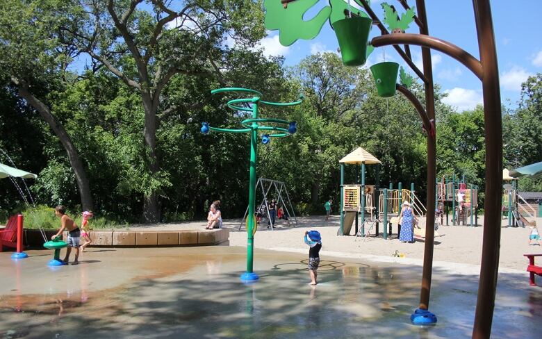 Children play at a splash pad near a playground outside on a sunny day