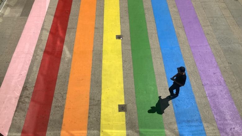 Someone walks across a rainbow crosswalk in front of Regina's Cornwall Centre.