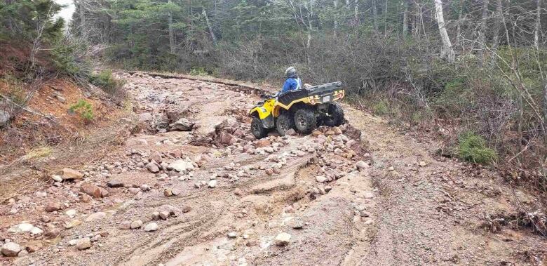 A yellow all-terrain vehicle with a person wearing a helmet on a dirt road full of rocks. 