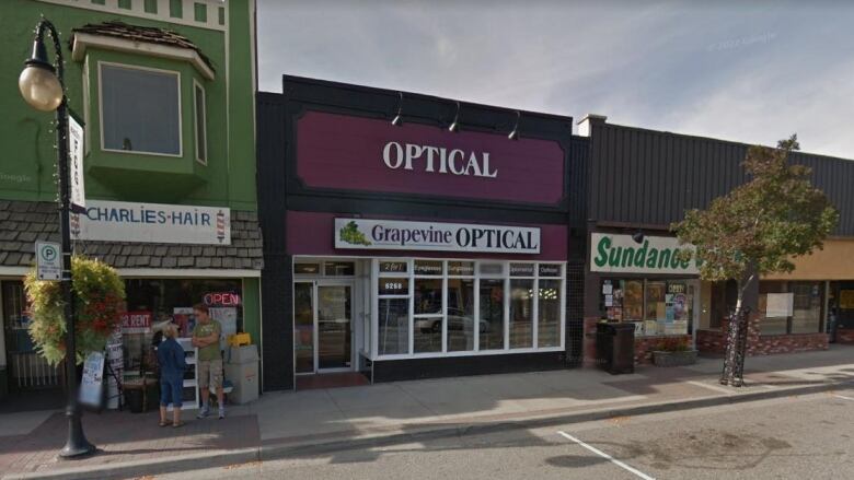 An optician's storefront on a street. The main sign, purple in colour, says 'Optical' in bold text. Underneath that, a smaller white sign says 'Grapevine OPTICAL' with a small clip art image of a bunch of grapes.