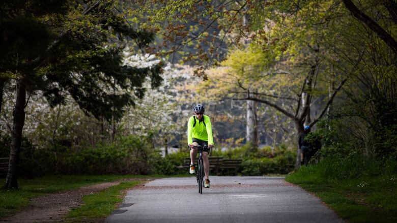 A man in a green high-visibility jacket rides a bicycle down a bike path.