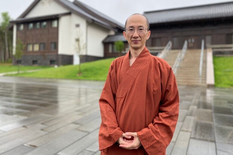 Man in orange robe stands in front of large residential building. 