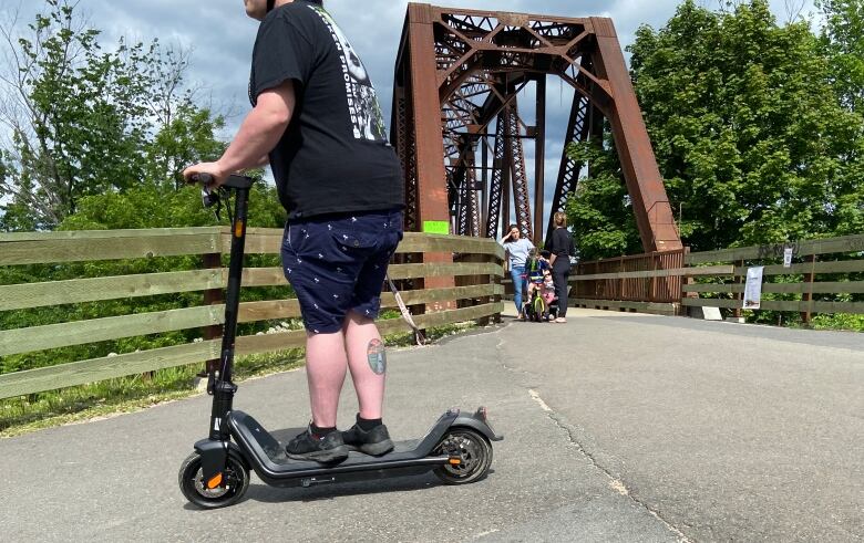 A person rides an electric scooter near the Bill Thorpe Walking Bridge in Fredericton.