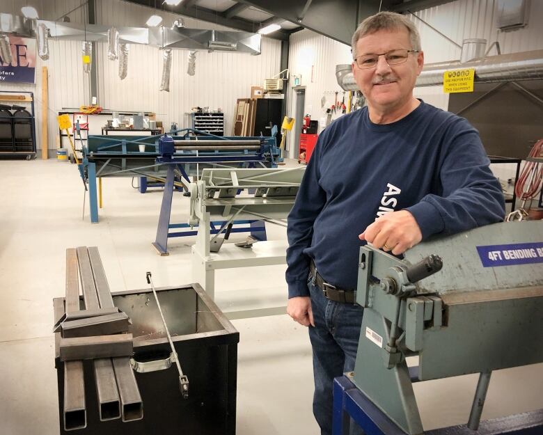 A man stands in a sheet metal workshop surrounded by equipment and tools.