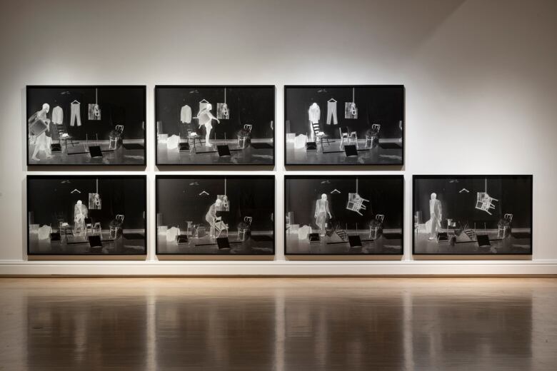 Seven large black and white photos installed on a white gallery wall.