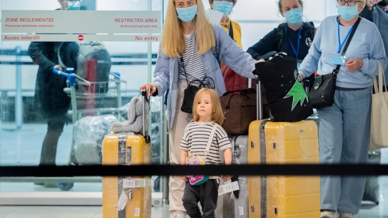 Several people carrying luggage walk through an airport.