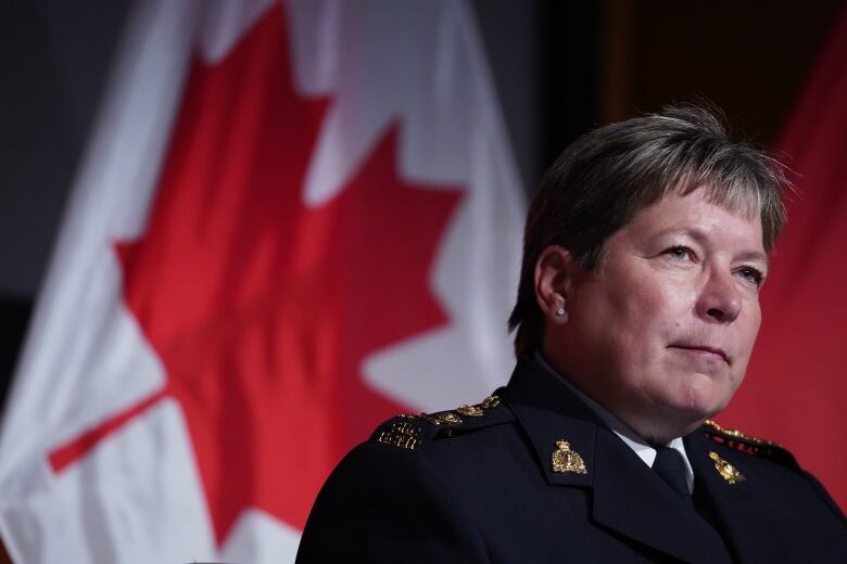 A woman in an RCMP uniform stands in front of a Canadian flag. 