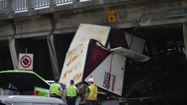 A crushed transport cab is stuck under a highway overpass.