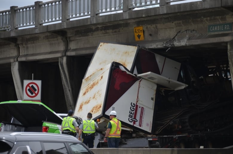 A crushed transport cab is stuck under a highway overpass.