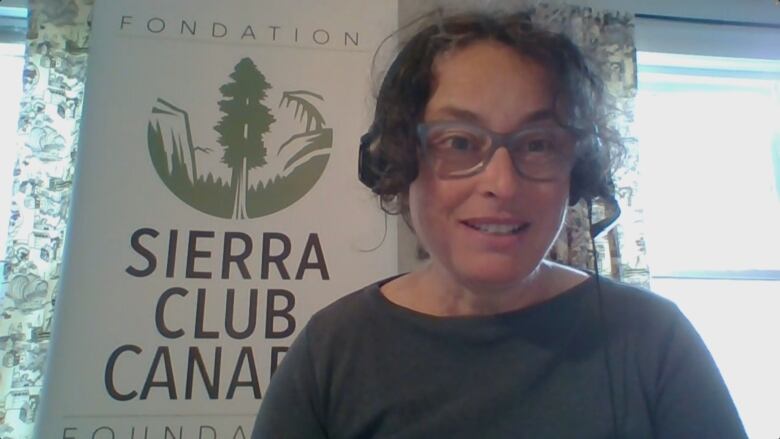 A woman wearing a headset sits in front of a banner for the Sierra Club Canada Foundation.