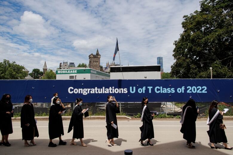 University students wearing gowns walk in a row in front of a banner saying 'Congratulations U of T Clads of 2022' 