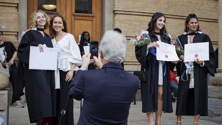 Three women take photos with their diplomas after a graduation ceremony.