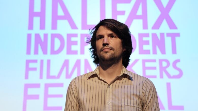 A man stands in front of a large projected screen that reads 'Halifax Independent Filmmakers Festival' in bold pink letters.