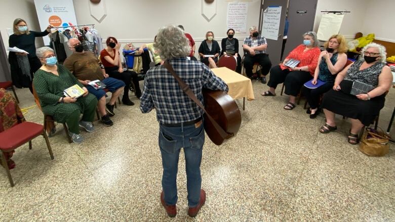 A man with a guitar stands in front of a group of people in a church basement.