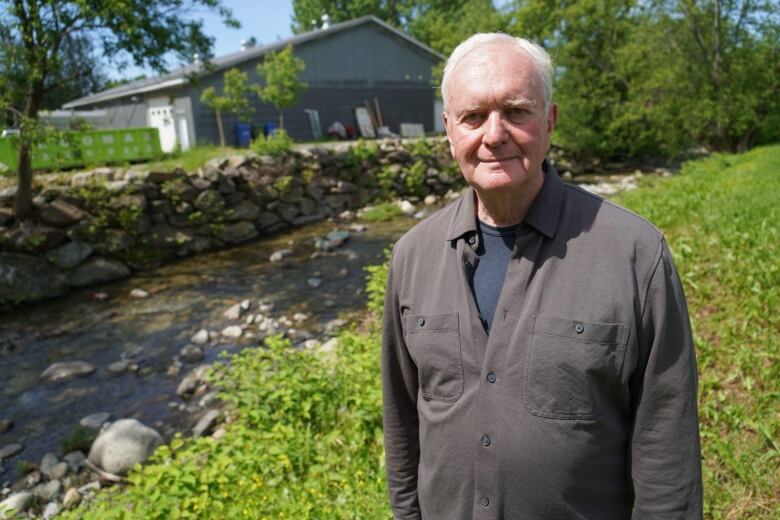 A man stands in a rural village, a house in the background.