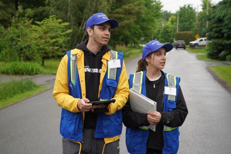 Two young people carrying pamphlets walk down a suburban street.