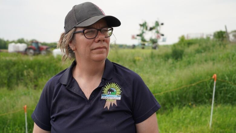 Woman in ball cap stands in a grassy field.