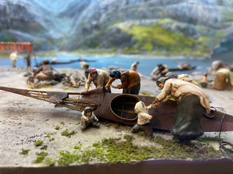 A model shows five miniature figures at a traditional kayak, which is balanced on its side. 