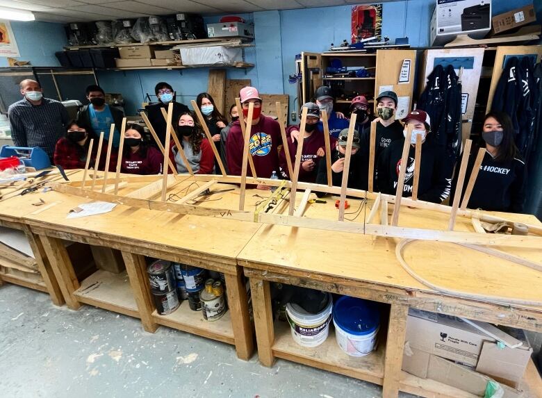 A workshop table in a school holds the frame of a kayak. Behind it are students who have been working on the construction project. 