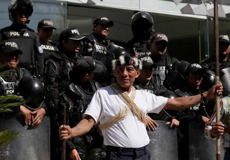 A member of the Waorani nation in a white t-shirt and head dress attends a protest.