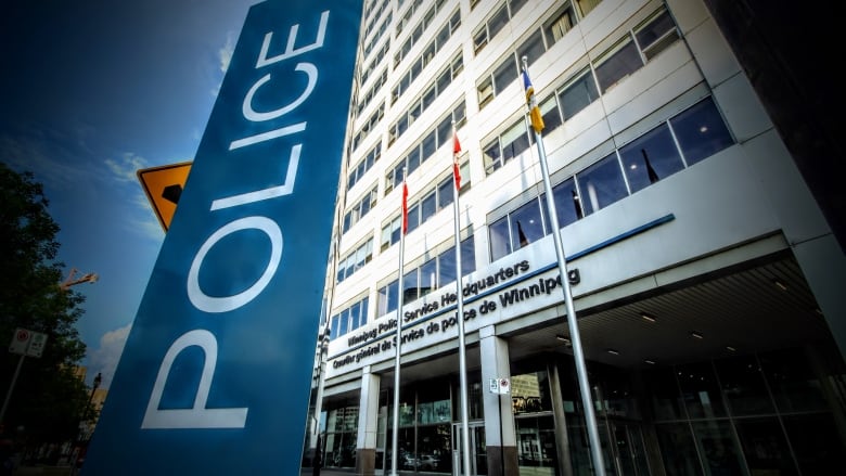 Photo shows a large building with flagpoles in the front and a large sign saying police on it. 