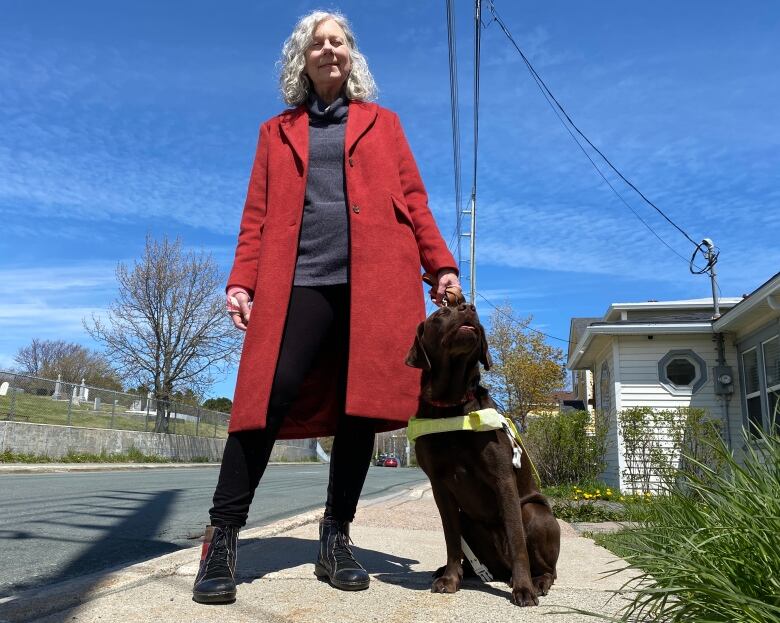 Anne Malone holds her guide dog, a chocolate Labrador named Purdy, while standing on a sidewalk. 