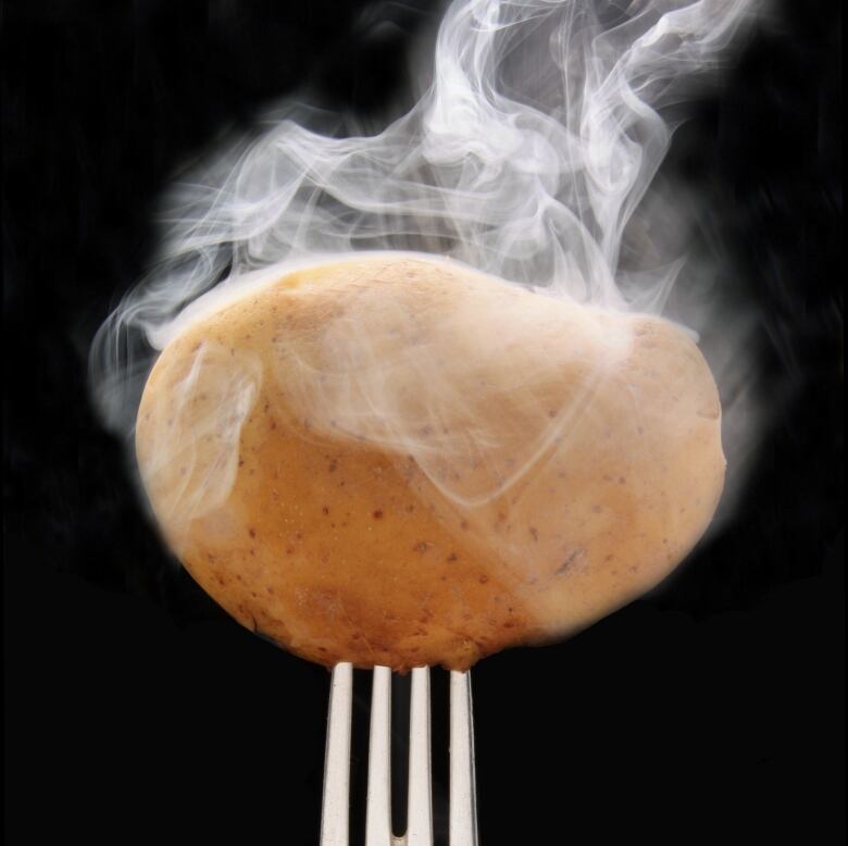 Steam rises from a cooked potato, which is held aloft by a fork. 