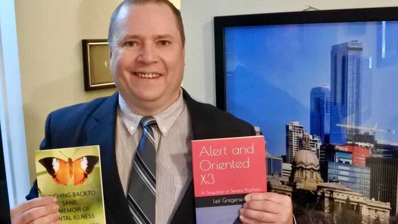 A smiling man holds two books.