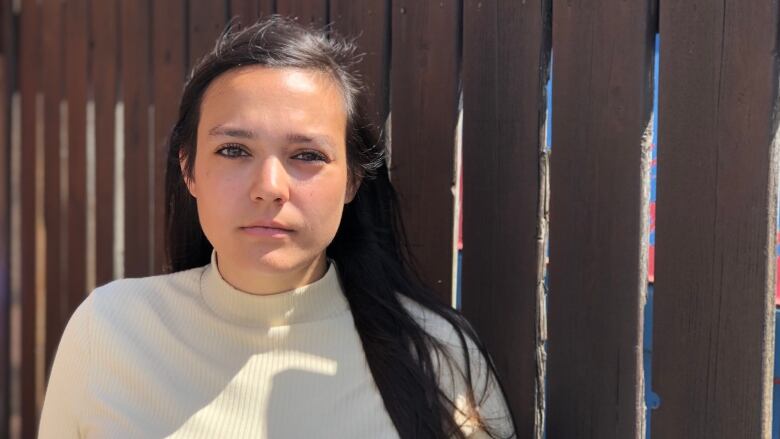 A young woman stands in front of a wooden fence.