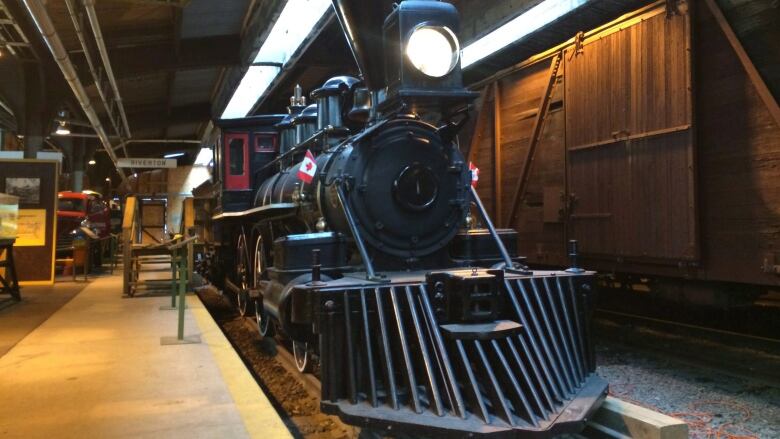 A steam locomotive with a bright headlight sits on a track at the Winnipeg Railway Museum.