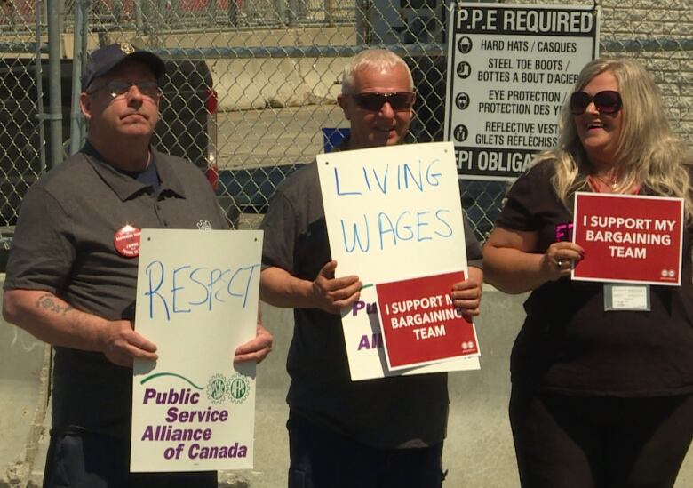 Three people stand in protest with signs that read 