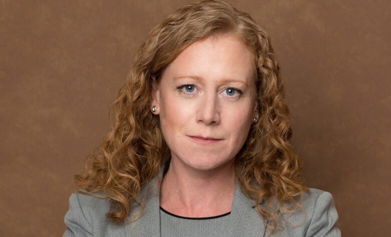 A woman with curly red hair poses for a professional headshot. She has a grey blazer on. 