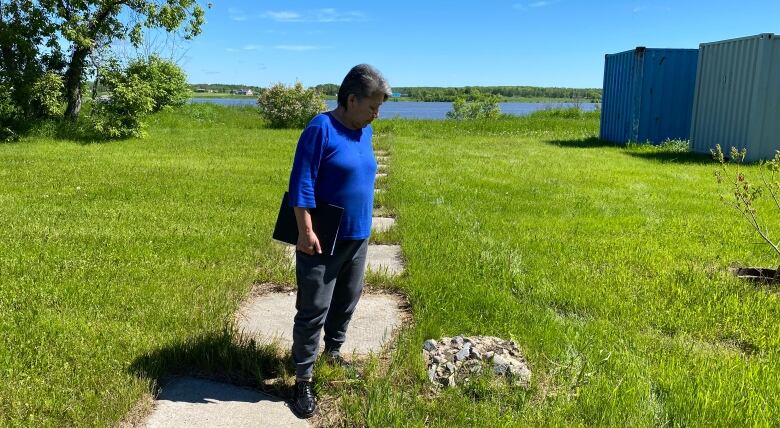 A woman stands in a grassy field amid stones that were part of the school.