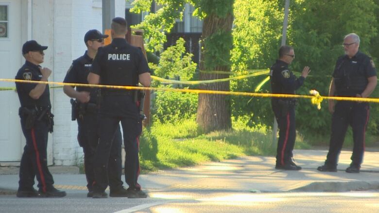 A group of police officers stands near yellow crime scene tape.